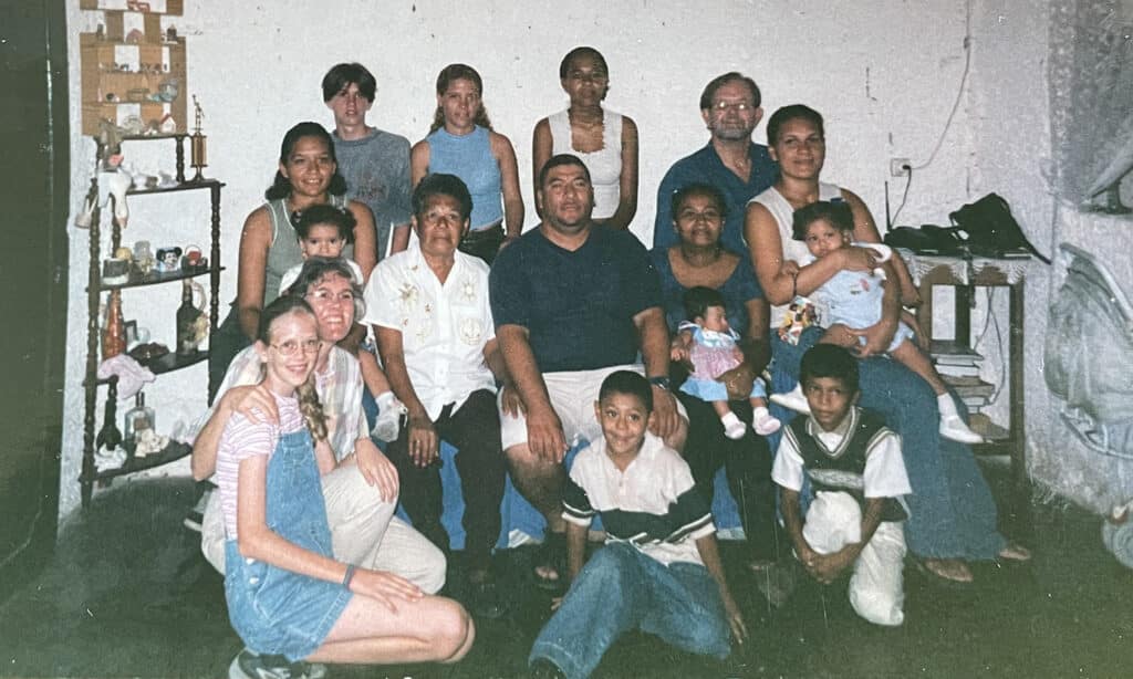 Multi-generational family group gathered indoors, posing together in a living room with adults, children, and babies.